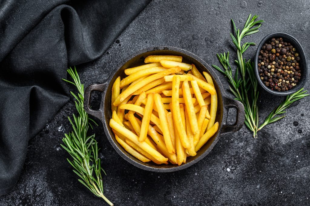 French fries in a pan, fried potatoes. Black background. Top view