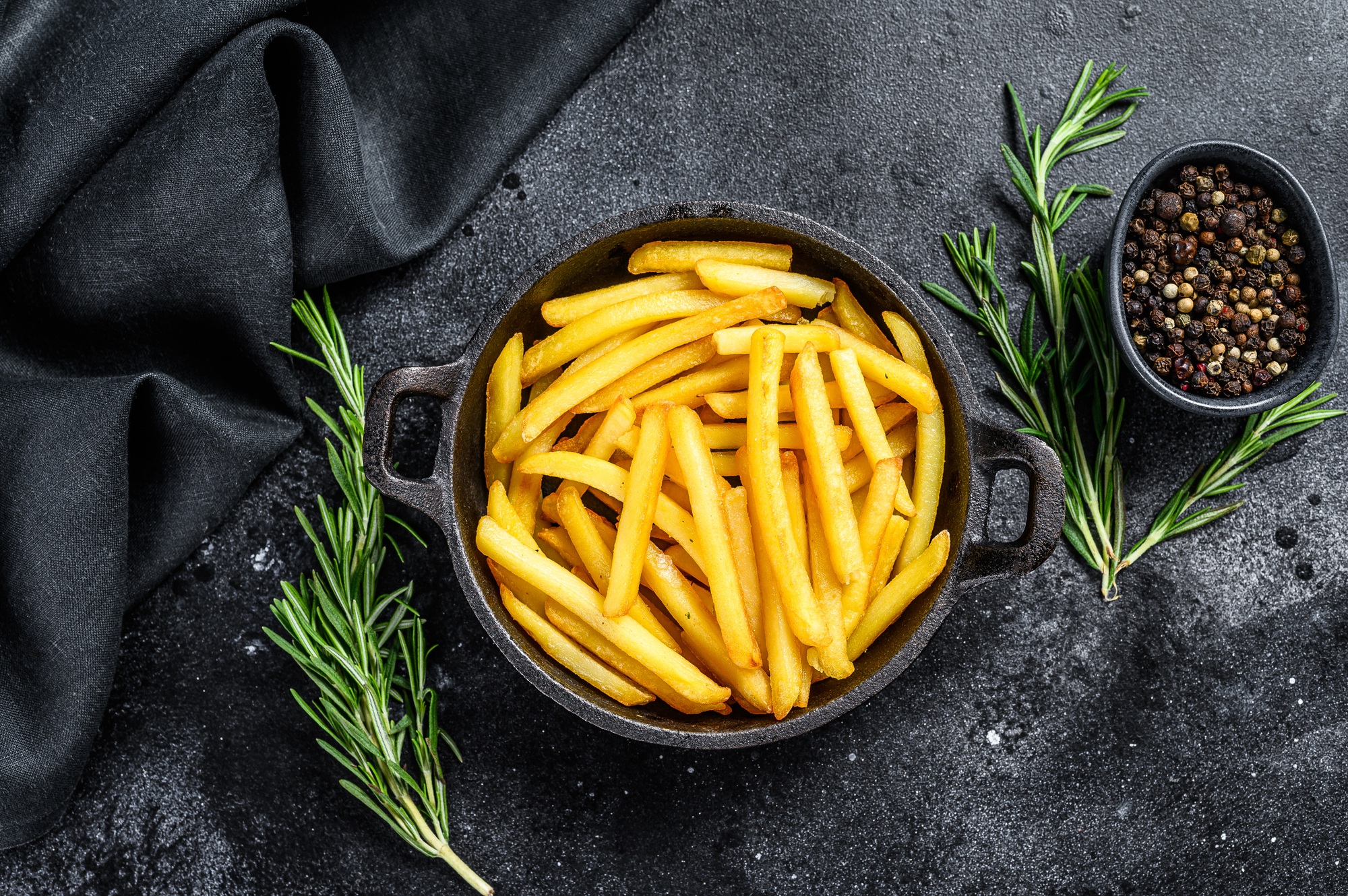 French fries in a pan, fried potatoes. Black background. Top view